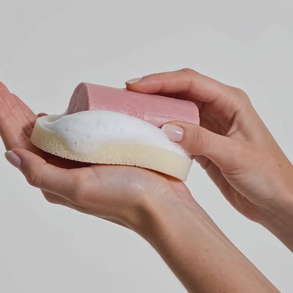 Mãos fazendo espuma com sabonete esfoliante em bastão Pink Color